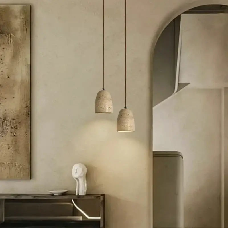 Two beige textured concrete decorbites led pendant lights with subtle perforations hanging from thin cords in yellow travertine