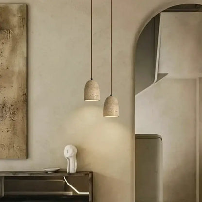 Two beige textured concrete decorbites led pendant lights with subtle perforations hanging from thin cords in yellow travertine