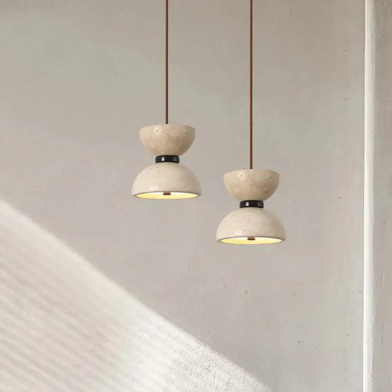 Two off-white textured stone decorbites led pendant lights with black metal accents and brown cords for living room use