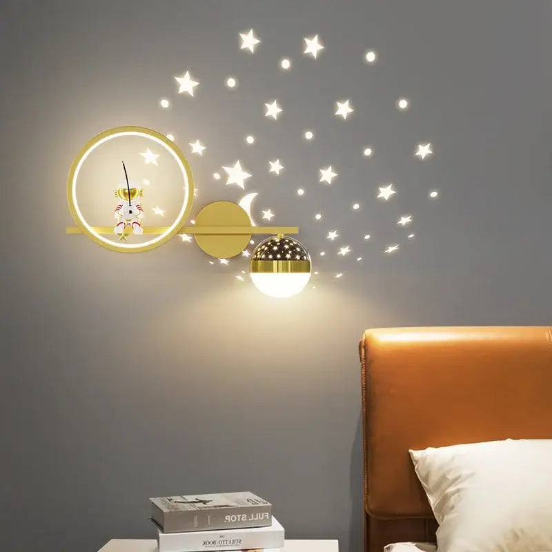 Gold-toned decorbites led star wall sconce with astronaut figurine and star cutout lampshade casting warm glow