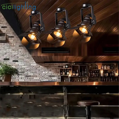 Three black decorbites led surface mount spotlights with warm amber glass shades hang from a wooden ceiling