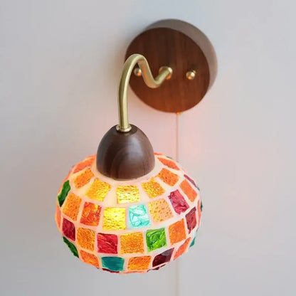 A vibrant decorbites led tiffany style wall sconce with colorful glass tiles on a brass arm and dark wood base
