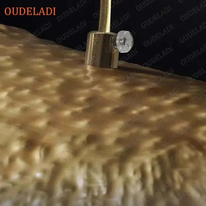Gold-colored metallic tuning peg with clear crystal knob on textured golden surface of decorbites lotus leaf copper pendant light