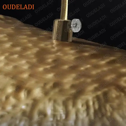 Gold-colored metallic tuning peg with clear crystal knob on textured golden surface of decorbites lotus leaf copper pendant light