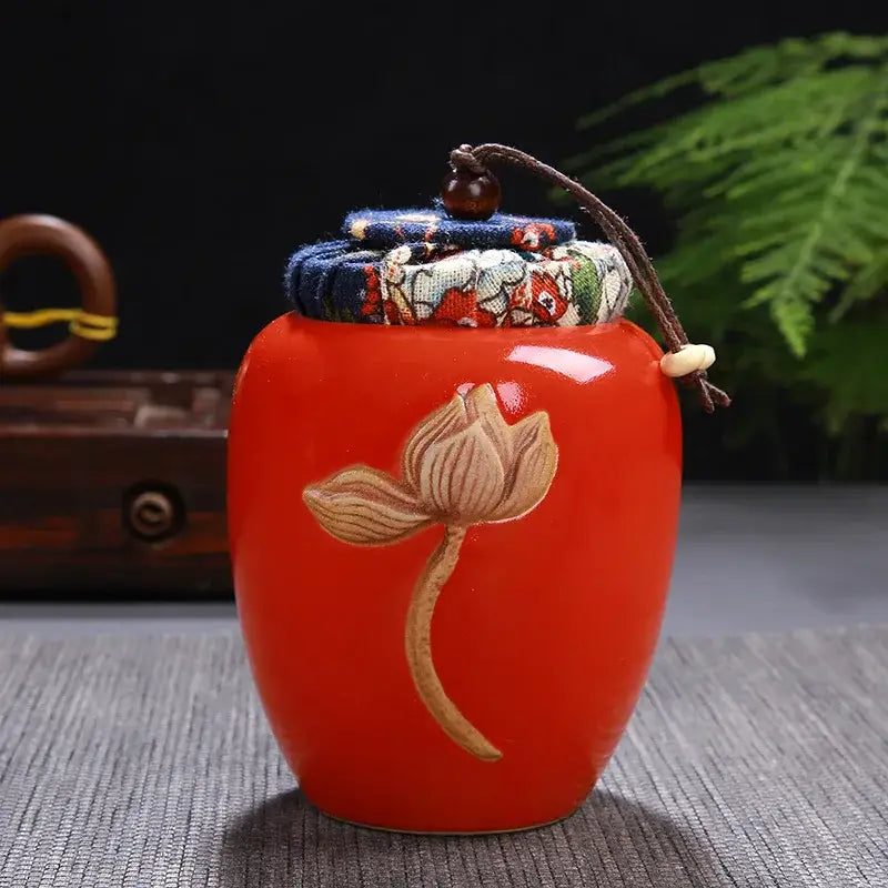 Vibrant red ceramic pot storage jar with hand-painted lotus pattern and fabric lid secured by brown cord for tea pot storage