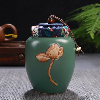 A jade-green ceramic pot storage jar with lotus pattern and fabric-lined lid secured by a brown cord for tea pot storage