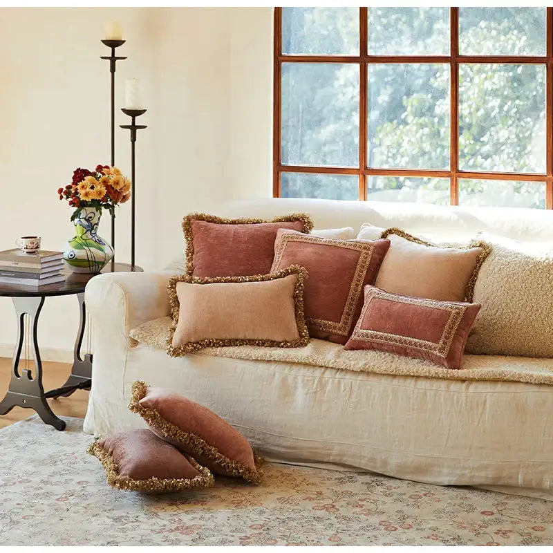 A collection of decorbites lotus pink velvet pillow covers in dusty rose and beige with gold-trimmed tassels on a cream sofa