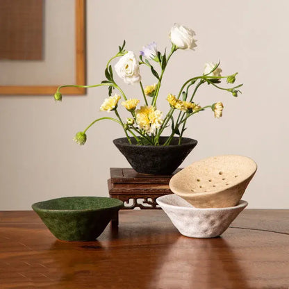 A dark textured lotus root clay bowl holding white and yellow flowers for home decor and terrarium use