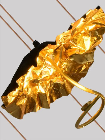 A crinkled gold foil umbrella with a black handle and golden metal frame in decorbites lotus staircase chandelier