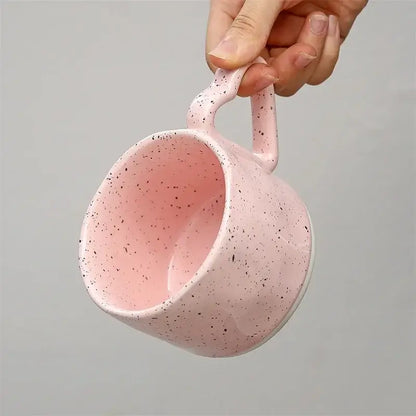 A pink speckled decorbites love handle ceramic cup held by hand ideal for breakfast tea coffee and office gifts