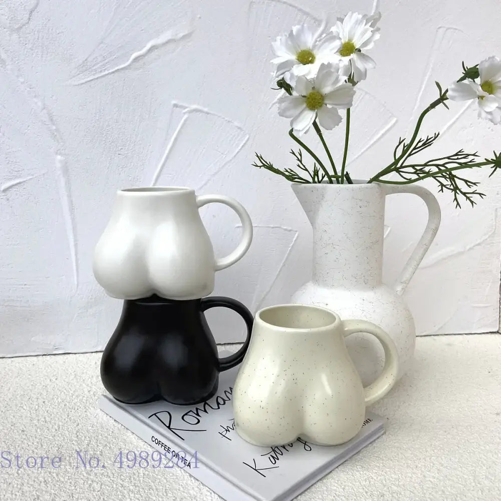 White ceramic coffee cup with playful sculpted buttocks shape and subtle speckled texture by DecorBites