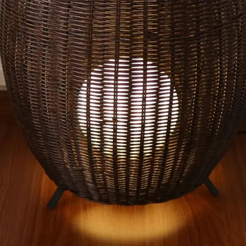 Dark brown woven wicker floor lamp with glowing white light decorbites lucide colin rattan for indoor use