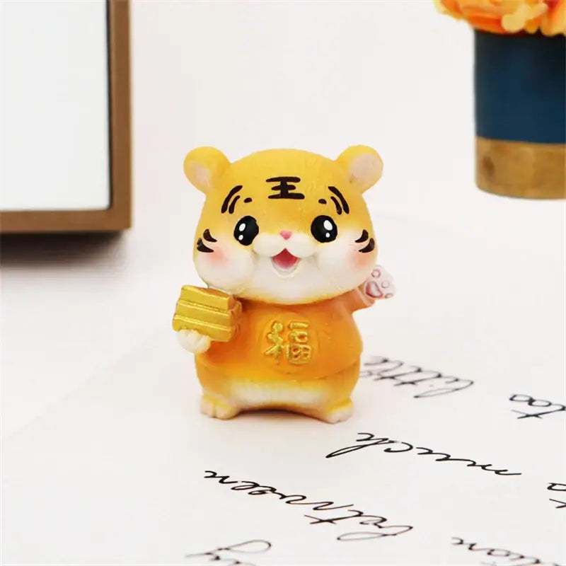 A cheerful yellow lucky tiger figurine holding golden bars and wearing an orange outfit with chinese characters