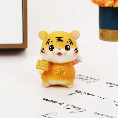 A cheerful yellow lucky tiger figurine holding golden bars and wearing an orange outfit with chinese characters