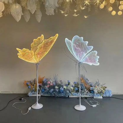 Two decorbites luminescent butterfly floor lamps glowing warm yellow and soft iridescent blue for wedding party decor