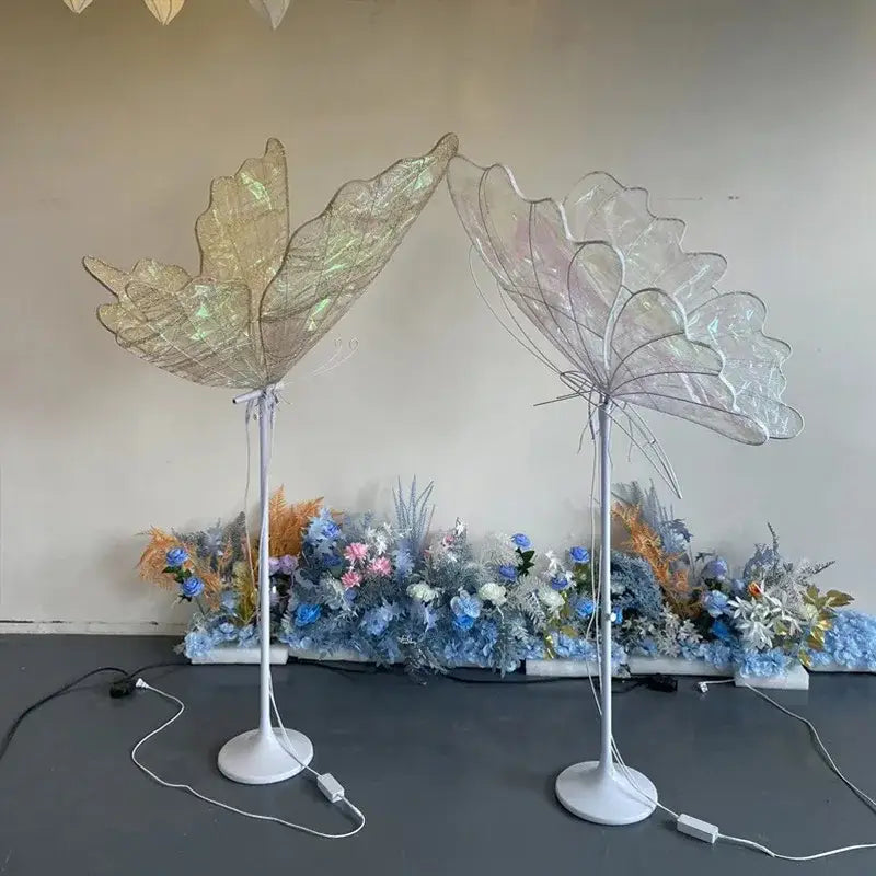 Two illuminated decorbites luminescent butterfly led floor lamps with translucent iridescent wings and white stands