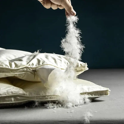 A hand pulls fluffy white down feathers from a cream decorbites luxe goose duck satin pillow for cozy warmth