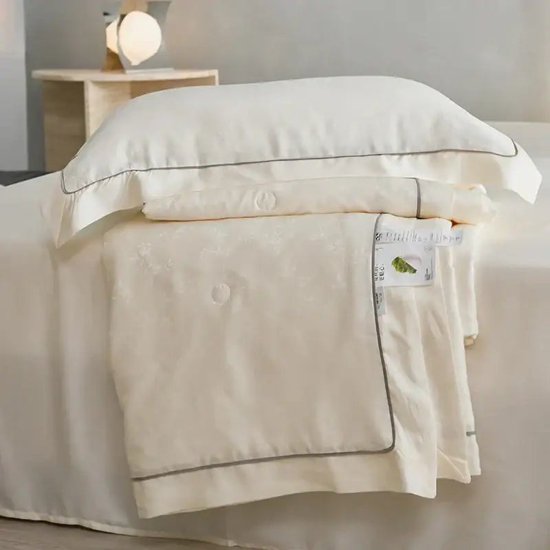 Cream-colored satin pillowcase with gray piping and matching quilted decorbites luxe lyocell summer blanket with mulberry silk fill