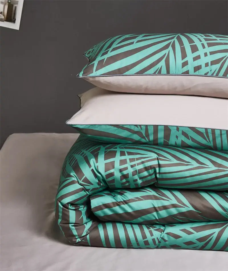 Stacked bedding set with teal and dark gray tropical leaf duvet cover and pieces pillowcases made of egyptian cotton satin fabric