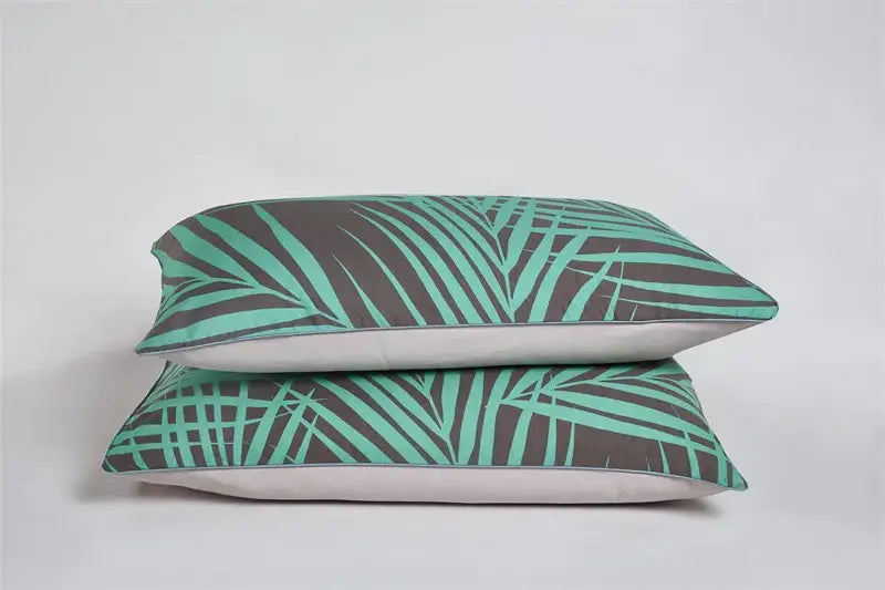 Two stacked rectangular pillows with teal and dark gray tropical leaf pattern and white linings from decorbites egyptian cotton bedding set
