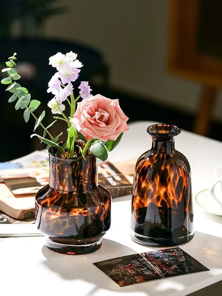 Two amber luxury leopard glass vases with tortoiseshell pattern, one holding pink and white flowers for home decor
