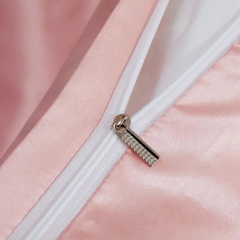 A silver-toned zipper pull with a textured pattern on the decorbites™ luxury solid color pcduvet cover in soft pink satin