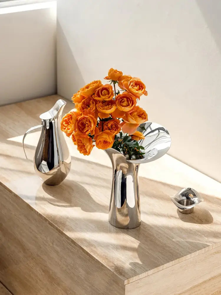 A luxury stainless steel vase by DecorBites with a sleek silver finish holding vibrant orange roses