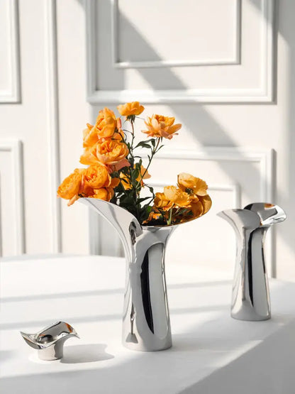 A sleek luxury stainless steel vase in silver holding vibrant orange roses for elegant home decor by decorbites