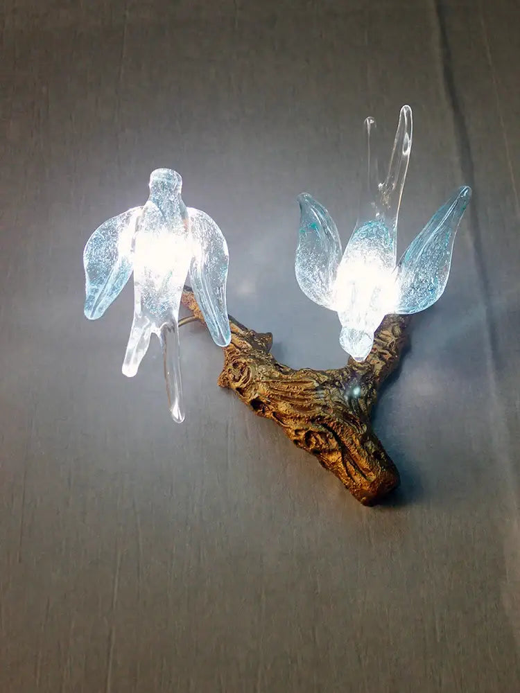 Two translucent blue glass birds with glowing interiors perch on a rustic branch in a decorbites luxury bird chandelier