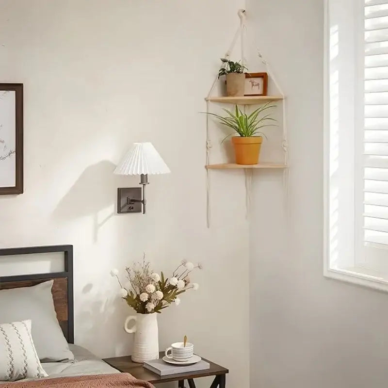 DecorBites™ lightweight wooden macrame wall hanging corner shelf with two tiers holding potted plants and a framed picture