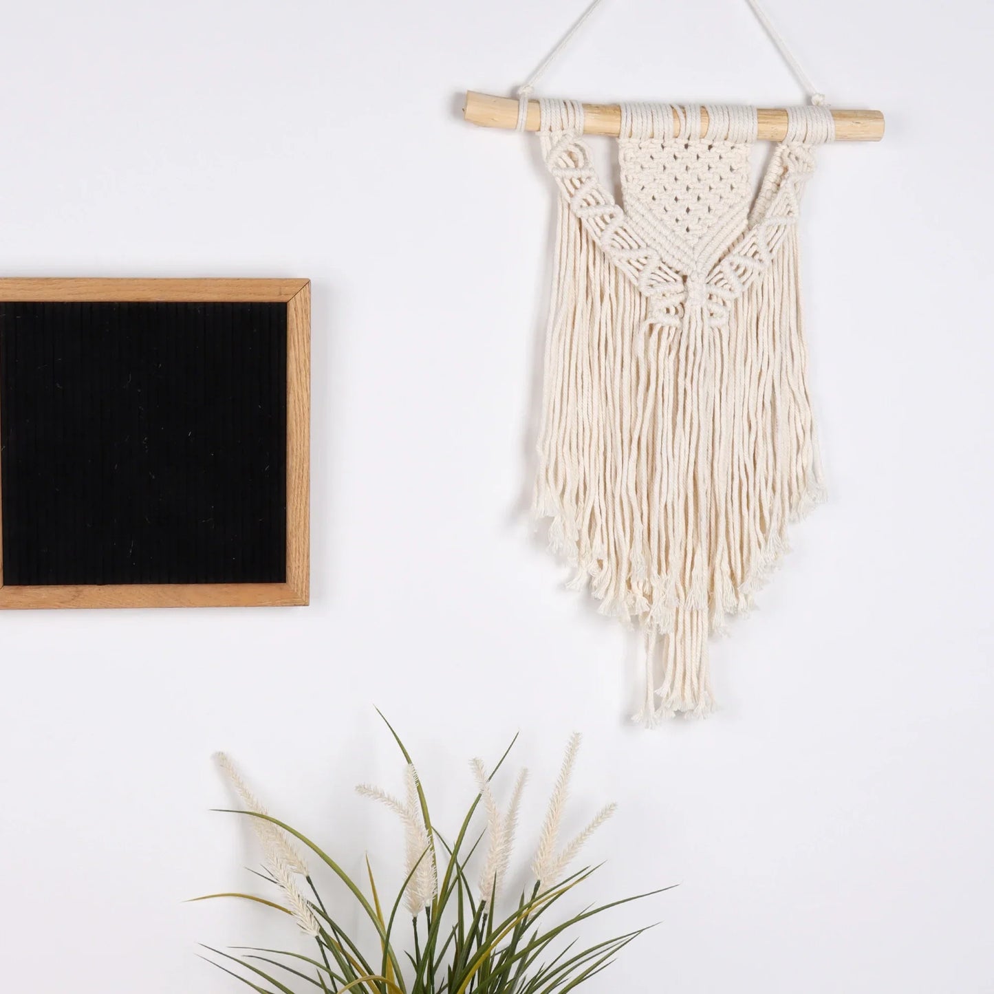 Cream-colored macrame wall hanging with wooden dowel and fringe for chic bohemian apartment and dorm room decor