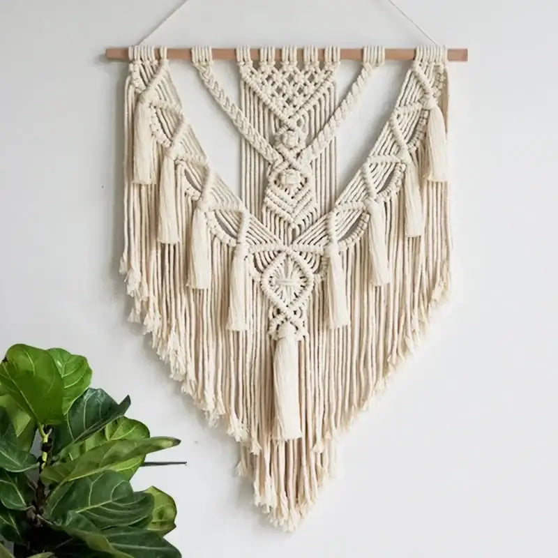 Cream-colored macrame wall hanging with intricate knotwork and fringe tassels for chic bohemian home decor
