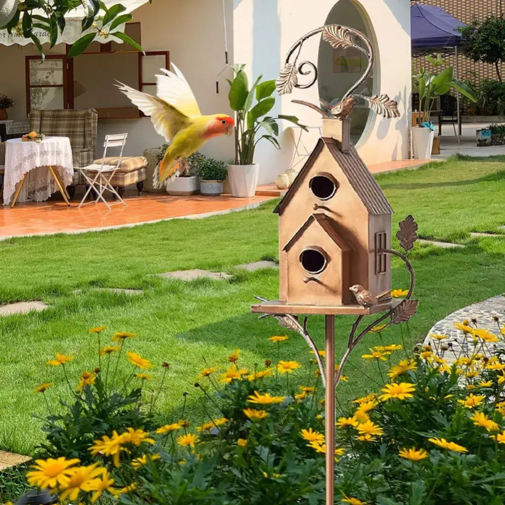 Rustic brown wooden birdhouse with metal leaf accents and curved roof on slender pole among yellow flowers for birdhouse garden stakes