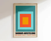 A framed DecorBites™ mid century geometric canvas wall art featuring concentric squares in teal, light blue, orange, and yellow