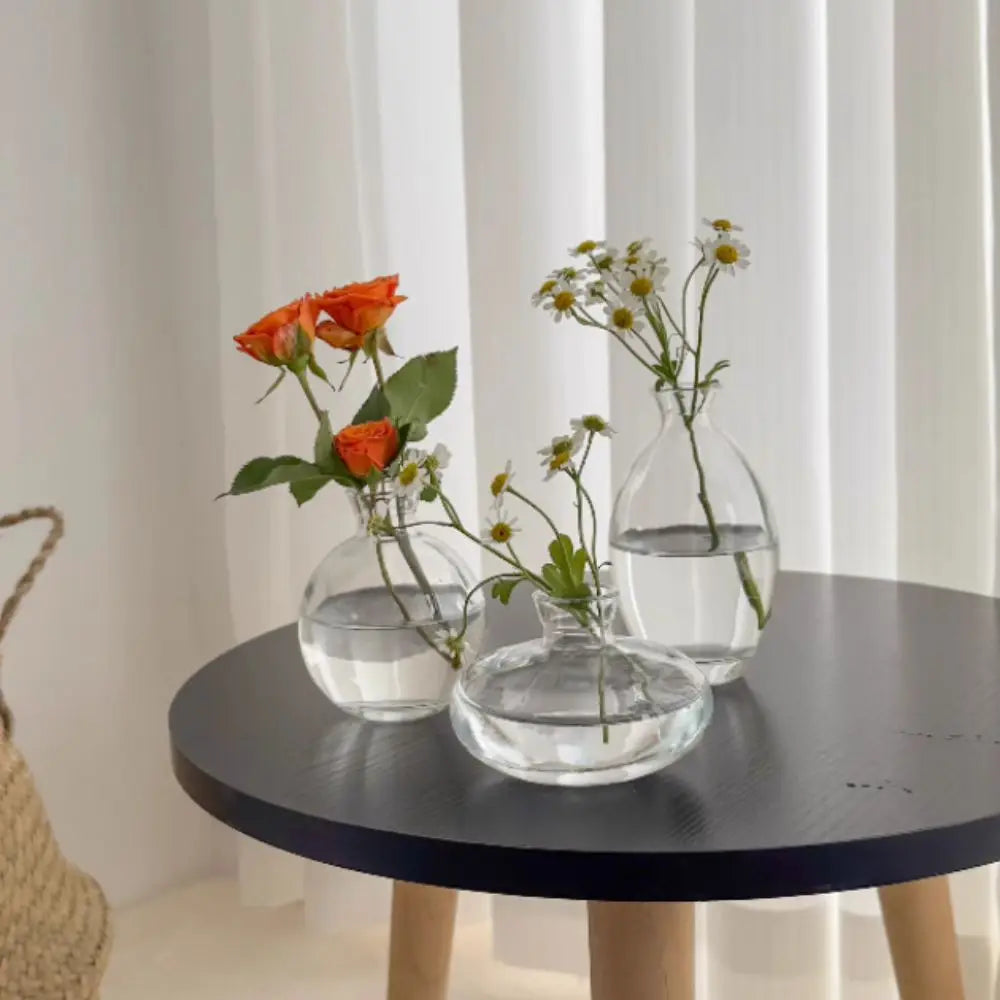 Three clear glass mini flower vases of varying shapes holding fresh flowers for home decor by decorbites