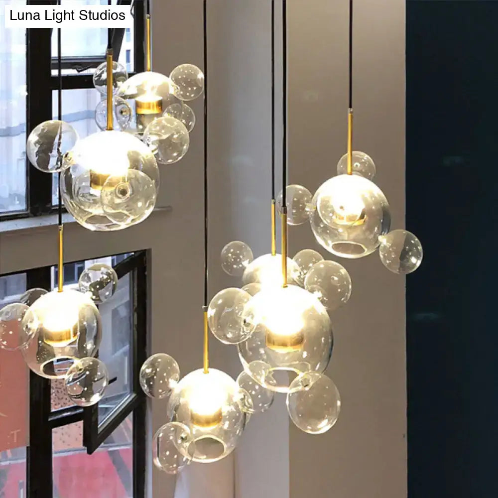 Modern pendant light featuring brass bubble design with five clear glass heads and gold-toned metal accents
