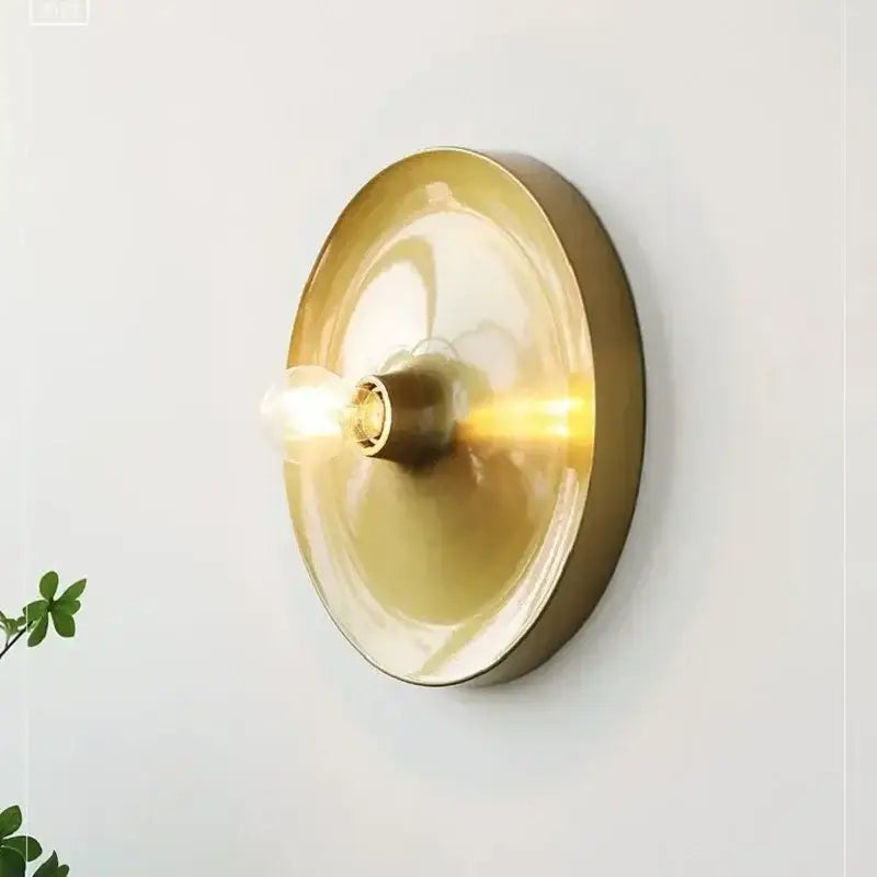 Brass-finished circular wall sconce with translucent amber glass shade and exposed bulb in decorbites bauhaus lamp style