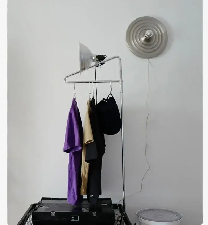 Silver metal clothing rack with hanging garments beside a studio light featuring the decorbites bauhaus lamp design