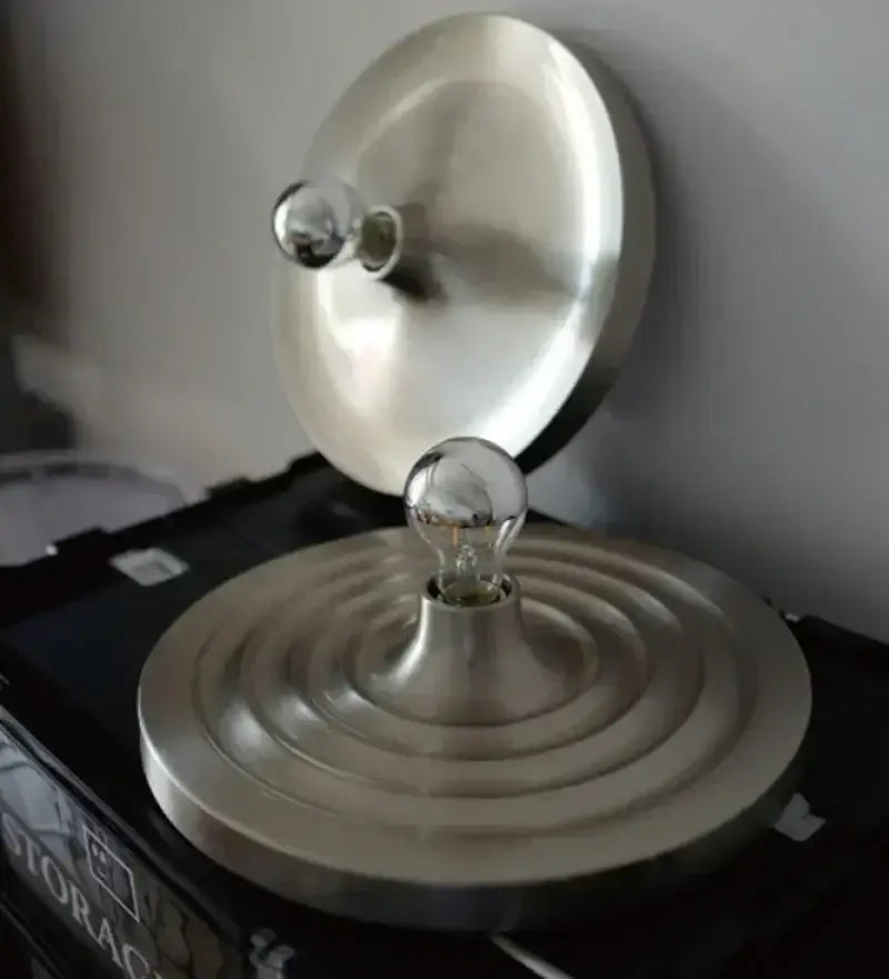 A sleek brushed metallic bauhaus lamp with circular base and two exposed glass bulbs by DecorBites Bauhaus