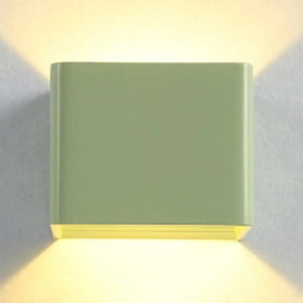 A sleek matte sage green decorbites minimalist cube sconce light with warm yellow glow for modern living room decor