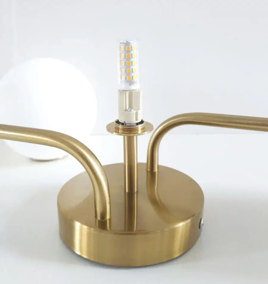 Gold-toned brass table lamp with minimalist curved arms and led bulb complementing decorbites™ acrylic ball ceiling light