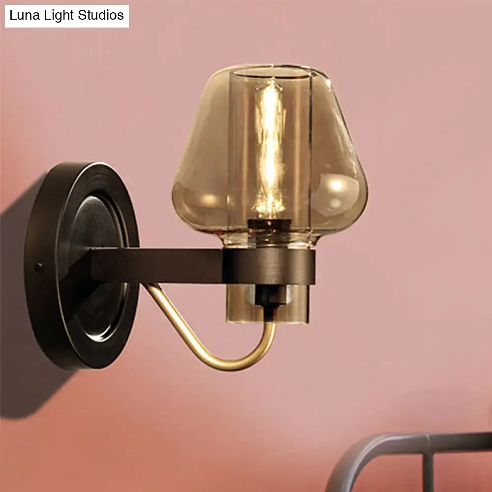 A modern black wall sconce with a dark bronze metal base and amber glass shade for bedroom lighting
