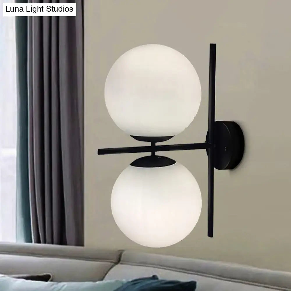 Modern black metal wall light fixture with two frosted white spherical glass shades for living room use