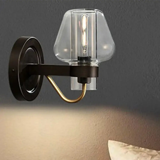 Modern black and brass wall sconce with a clear glass mushroom shade and exposed filament bulb for bedroom use