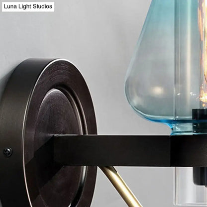 Modern blue glass wall sconce light fixture with tapered shade mounted on black metal arm with brass accents for bedroom wall