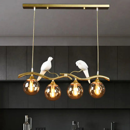 Gold-toned metal island pendant light with curved branch design and white ceramic birds holding amber glass globe bulbs