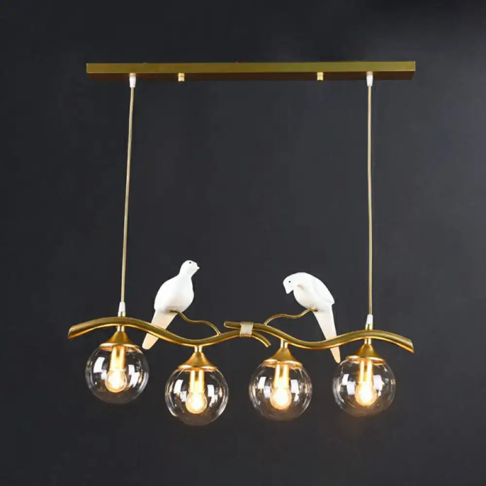 Gold-toned metal island pendant light with four glass bulbs and two white ceramic birds on a curved branch design