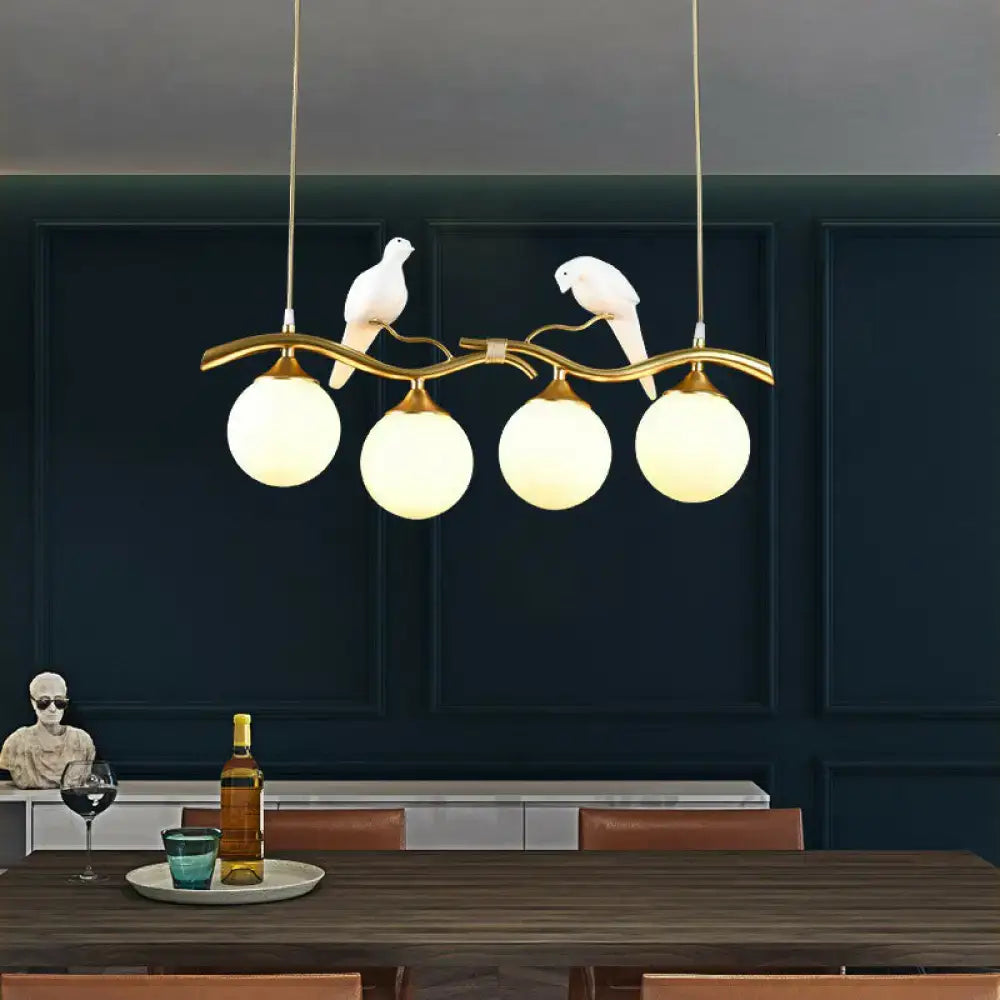 Gold-toned metal DecorBites modern island pendant light with curved branch design, white bird figurines, and frosted glass globes
