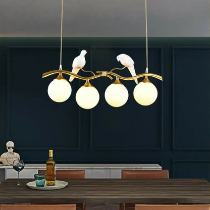 Gold-toned metal DecorBites modern island pendant light with curved branch design, white bird figurines, and frosted glass globes