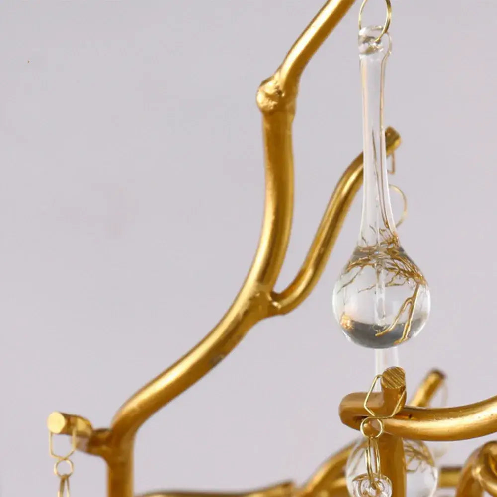 A clear glass teardrop pendant with gold wire details hanging from a golden branch frame in a modern chrome crystal chandelier for living room